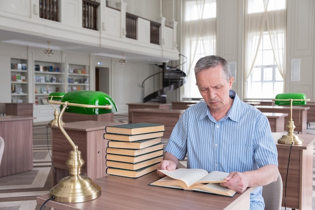 Portrait d'un homme senior caucasien travaillant avec un livre dans une bibliothèque publique