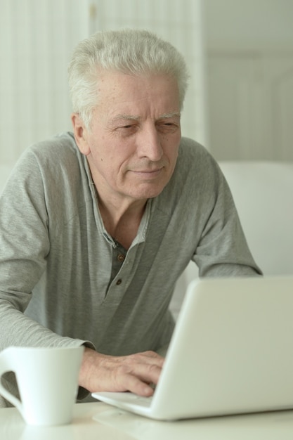 Portrait d'homme senior dans la cuisine à la maison avec ordinateur portable