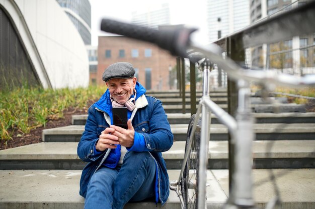 Portrait d'un homme senior heureux avec un vélo à l'extérieur en ville, prenant un selfie.