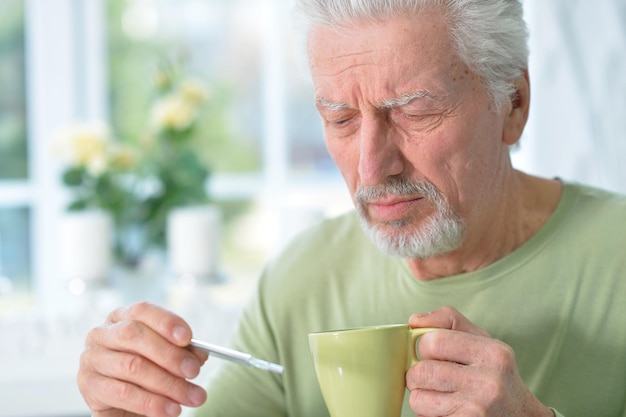 Portrait d'homme senior malade triste avec thermomètre à la maison