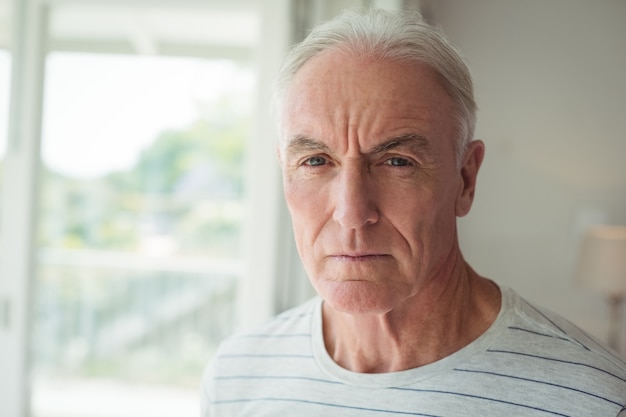 Portrait d'un homme senior réfléchi debout à côté de la fenêtre