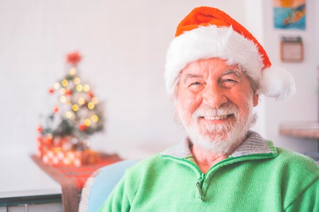 Portrait d'un homme senior à la retraite souriant en bonnet de noel et des vêtements chauds célébrant Noël à la maison. Vieux père Noël souriant tout en regardant la caméra. Homme âgé profitant des vacances de Noël