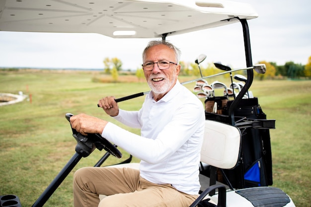 Portrait d'un homme senior riche conduisant une voiture de golf jusqu'à la zone verte pour continuer à jouer.