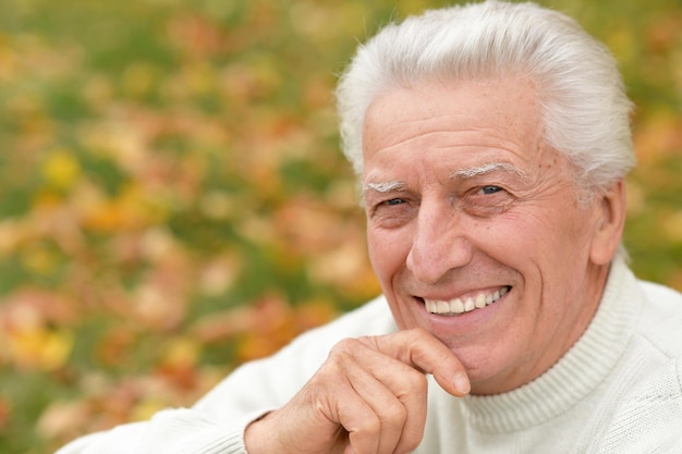 Portrait d'un homme senior souriant à l'extérieur tenant la main sur le menton