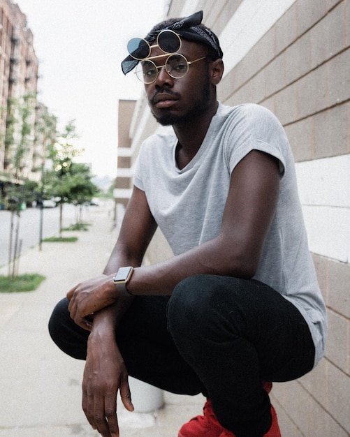 Photo portrait d'un homme sérieux accroupi sur le trottoir contre un bâtiment