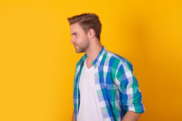 Portrait d'homme sérieux debout sur le côté en chemise à carreaux profil de fond jaune