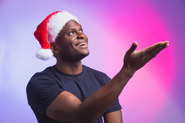 Portrait d'un homme souriant afro-américain positif en bonnet de noel et t-shirt décontracté sur coloré