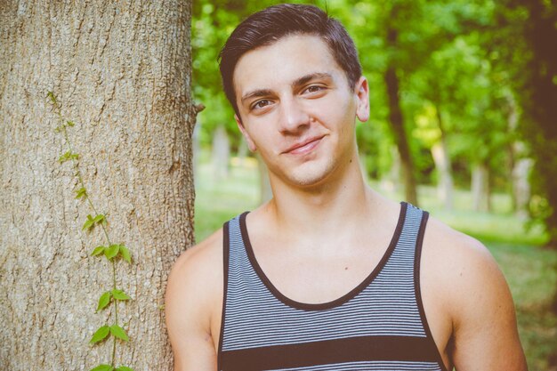 Portrait d'un homme souriant appuyé sur un arbre dans un parc