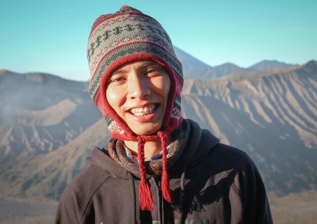 Photo portrait d'un homme souriant dans un chapeau tricoté contre les montagnes