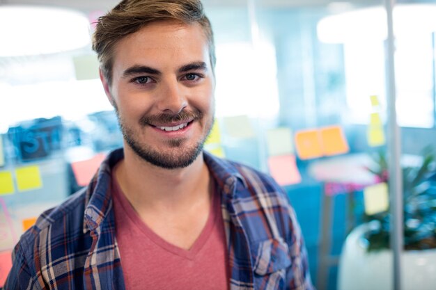 Portrait d'homme souriant debout contre des notes autocollantes sur le mur de verre au bureau