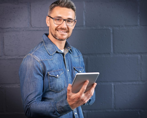 Portrait d'un homme souriant et d'une tablette par un mur de briques pour l'information de communication en ligne et les médias sociaux Programmateur masculin heureux et technologue pour la connexion de mise à jour du système et le lien vers le site Web par un fond sombre