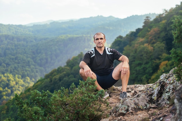 portrait d'un homme sportif fort qui s'assied sur la pente d'une haute montagne et se repose