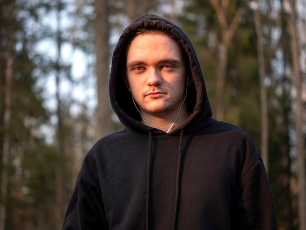 Portrait d'un homme en survêtement noir avec fond de forêt floue