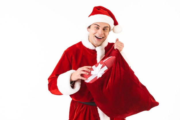 Portrait d'un homme sympathique des années 30 en costume de père Noël et chapeau rouge tenant un sac de fête avec boîte-cadeau