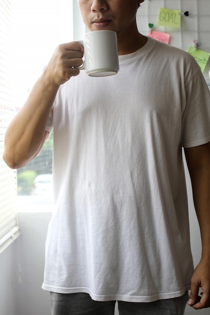 Portrait d'un homme en t-shirt uni tenant une tasse en porcelaine pour une maquette