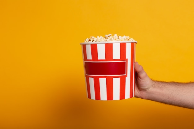 Portrait de l'homme tenant un seau avec du pop-corn sur jaune