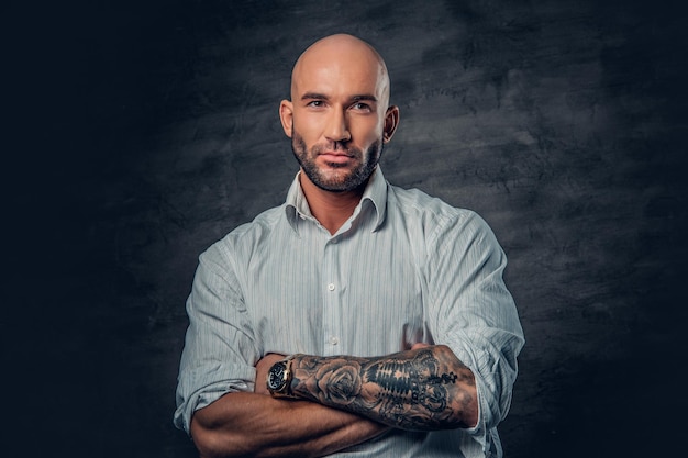 Portrait d'homme à la tête rasée dans une chemise blanche avec des bras croisés tatoués.