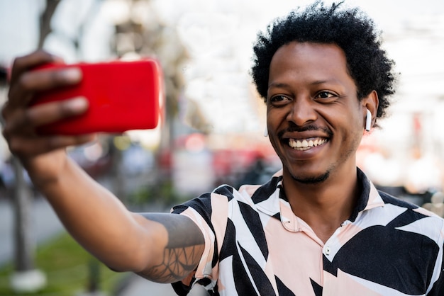 Portrait d'homme de tourisme afro prenant un selfie avec téléphone à l'extérieur dans la rue.