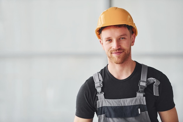 Portrait d'un homme en uniforme gris et casque orange qui se tient à l'intérieur dans un grand bureau moderne pendant la journée