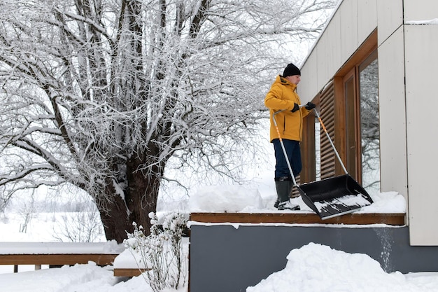 Portrait d'un homme en vêtements d'hiver avec pelle à neige nettoyant la neige depuis la terrasse de l'immeuble