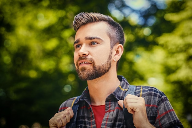 Portrait d'homme voyageur barbu vêtu d'une chemise polaire sur fond de parc sauvage.