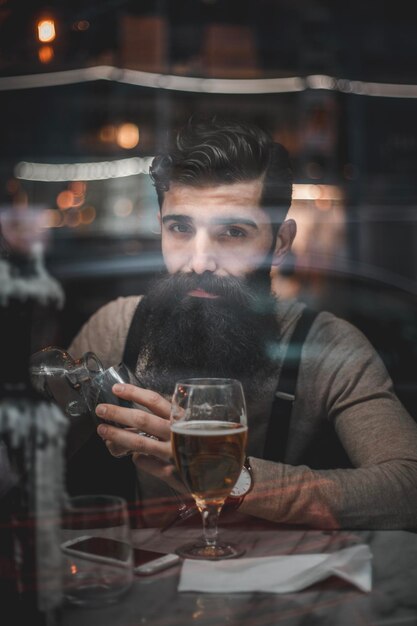 Photo portrait d'un homme vu à travers une fenêtre en verre tenant un verre alors qu'il est assis dans un restaurant