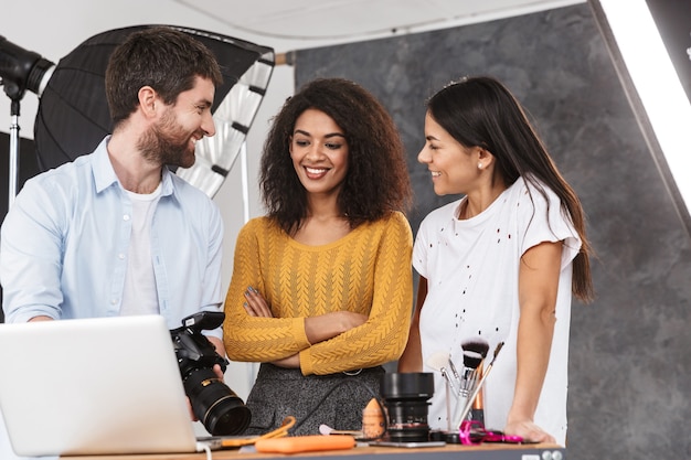 Portrait d'hommes et de femmes multiethniques heureux regardant un ordinateur portable pendant une prise de vue avec un appareil photo professionnel en studio