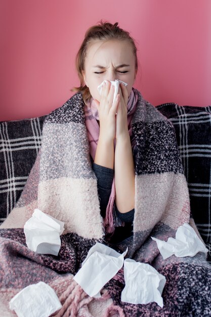 Portrait horizontal jeune fille avec un mouchoir et nez qui coule de profil, éternuements de grippe, modèle féminin à peau blanche au mur rose. Concept de soins de santé et médical.
