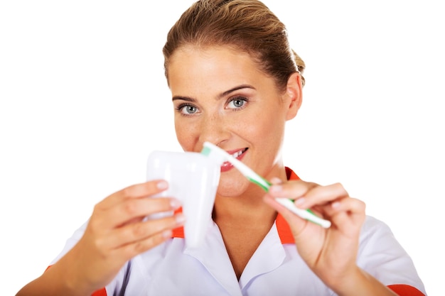 Photo portrait d'une infirmière tenant une prothèse dentaire avec une brosse à dents alors qu'elle se tient sur un fond blanc