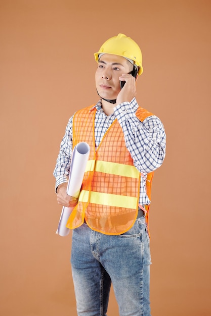 Portrait d'ingénieur en construction sérieux avec plan à la main parlant au téléphone avec l'entrepreneur