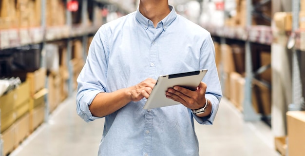 Portrait d'ingénieur contremaître homme commande les détails vérifiant les marchandises sur tablette et les fournitures sur les étagères avec l'arrière-plan des marchandises dans l'entrepôt logistique et l'exportation commerciale