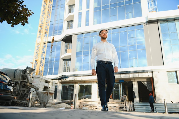 Photo portrait d'ingénieur homme au chantier. directeur de construction masculin portant un casque blanc et un gilet de sécurité jaune