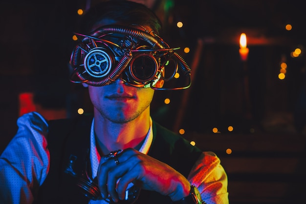 Portrait d'un ingénieur masculin dans des lunettes cyberpunk et un costume steampunk dans un atelier avec un néon