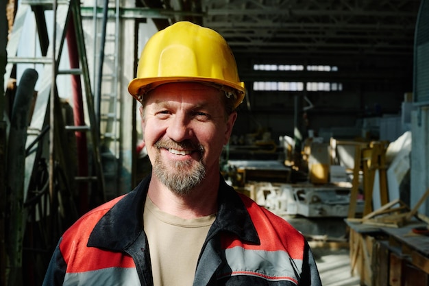 Portrait d'ingénieur mature en casque de travail souriant à la caméra debout dans l'atelier de l'usine