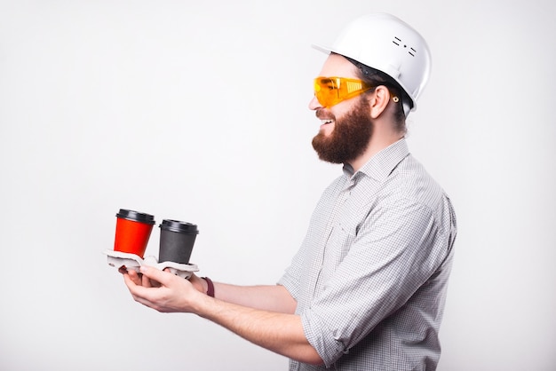 Portrait d'ingénieur souriant portant un casque blanc et donnant du café à emporter aux travailleurs ou collègues