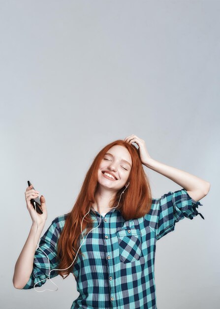 Portrait insouciant et heureux d'une jeune femme rousse joyeuse et jolie dans des écouteurs écoutant de la musique