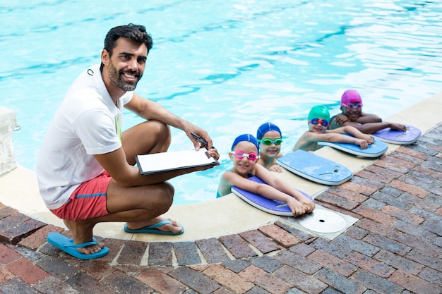 Portrait de l'instructeur masculin avec de petits nageurs au bord de la piscine