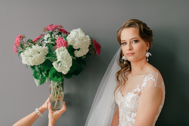 Portrait intérieur de belle jeune mariée avec les mains tenant un vase avec des fleurs près.