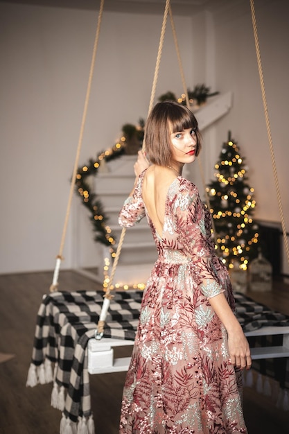 Portrait intérieur d'une fille confiante dans une longue robe posant près de l'arbre de Noël. Mise au point douce. Mise au point sélective.
