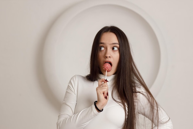 Portrait intérieur d'une jeune femme brune souriante positive sur fond blanc tenant un gâteau de dessert sucré dans les mains