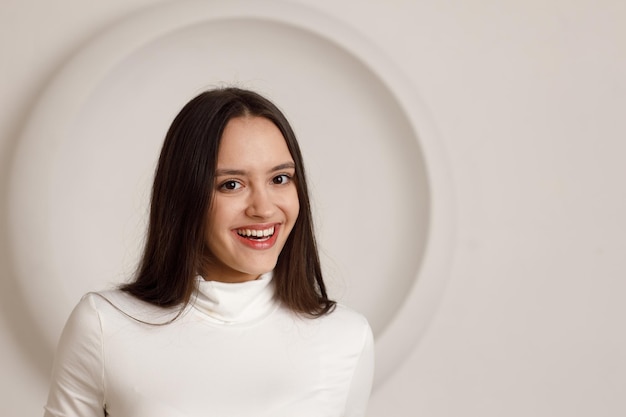 Portrait intérieur d'une jeune femme brune souriante positive sur fond blanc