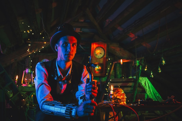 Portrait d'un inventeur masculin en costume steampunk, un chapeau haut de forme avec une canne à la main se trouve dans un atelier de montres avec néon. Cosplay cyberpunk