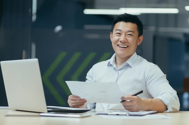 Photo portrait d'un investisseur asiatique prospère derrière la paperasse homme d'affaires travaillant dans un bureau moderne tenant