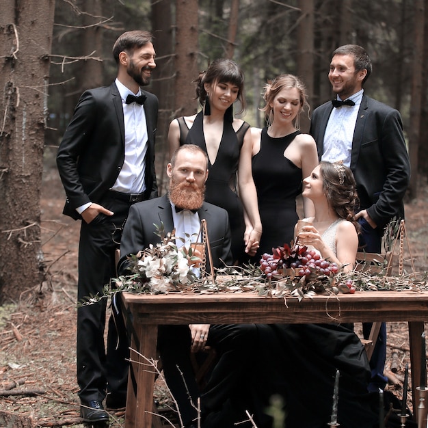 Portrait d'un invité et d'un couple de jeunes mariés près d'une table de pique-nique dans les bois