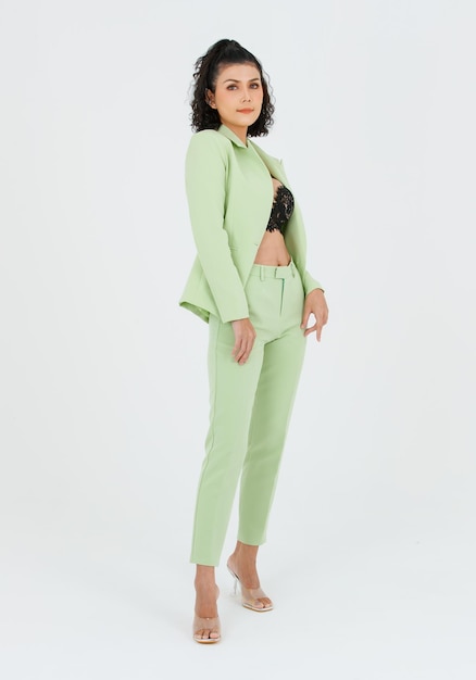 Portrait isolé coup de studio de découpe de femme d'affaires de mode asiatique sexy cheveux bouclés en costume vert avec lingerie en dentelle noire soutien-gorge haut court debout posant mettre les mains dans les poches du pantalon sur fond blanc