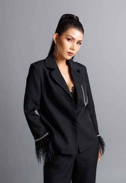 Portrait isolé coup de studio de découpe de modèle de mode élégante femme asiatique millénaire en costume de fourrure à la mode décontracté noir debout posant mettre la main dans la poche du pantalon regarder la caméra sur fond gris