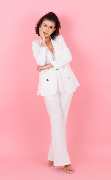 Portrait isolé découpe studio tourné asiatique sexy coiffure bouclée succès femme d'affaires en costume décontracté à la mode blanc avec dentelle lingerie haut court soutien-gorge debout posant bras croisés sur fond rose