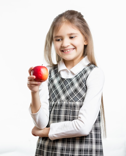 Portrait isolé d'une écolière souriante regardant une pomme rouge