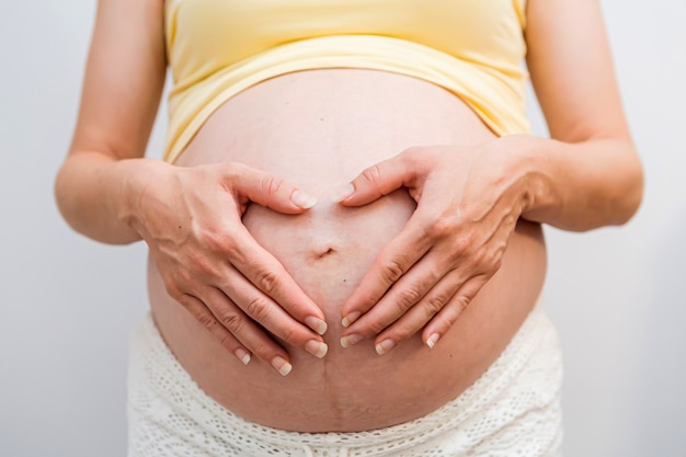 Portrait isolé d'une femme enceinte, tenant ses mains en forme de cœur sur son bébé bosse sur fond blanc