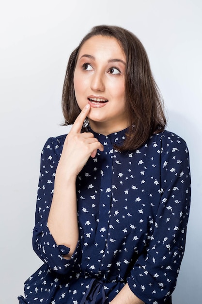 Portrait isolé d'une jeune femme métisse élégante aux cheveux noirs touchant son menton et levant les yeux, sur le côté avec une expression douteuse et sceptique, soupçonnant